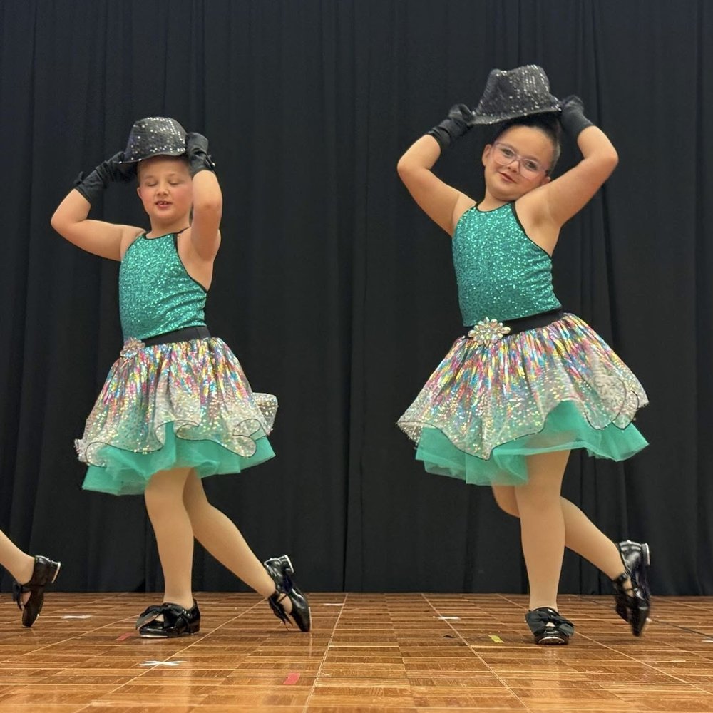 Two dancers in sparkly recital costumes performing on stage