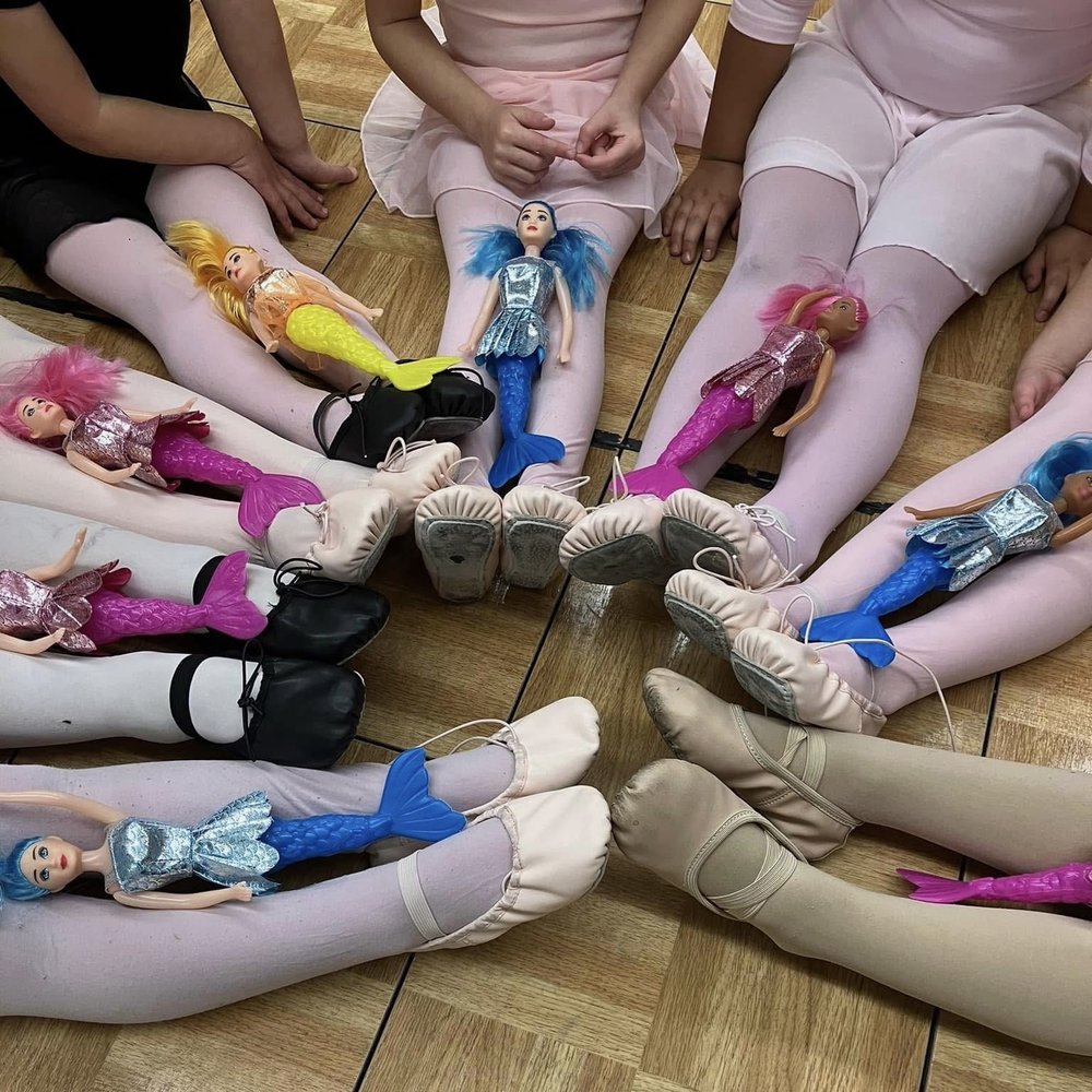 Ballet students sitting in a circle with their dance shoes and toy mermaid dolls