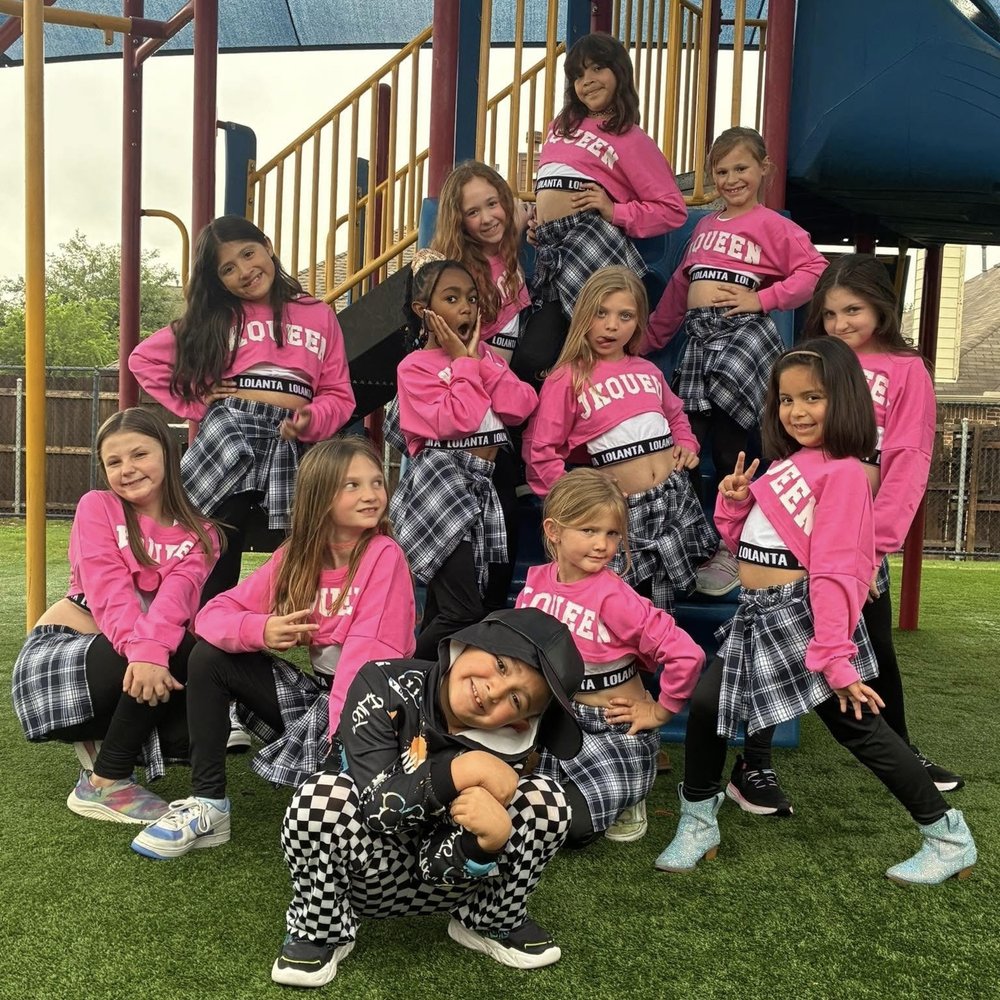 A large group of young dancers in matching pink outfits posing outdoors